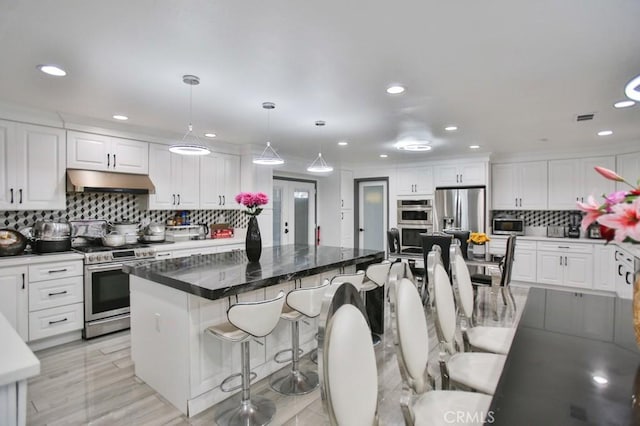 kitchen with decorative light fixtures, appliances with stainless steel finishes, white cabinetry, and a center island