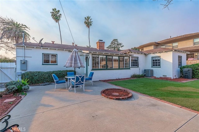 back house at dusk featuring a patio area, central AC, a fire pit, and a lawn