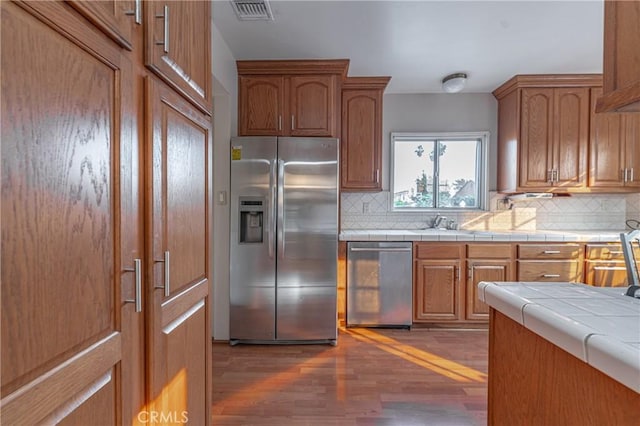 kitchen featuring appliances with stainless steel finishes, dark wood-type flooring, sink, backsplash, and tile countertops