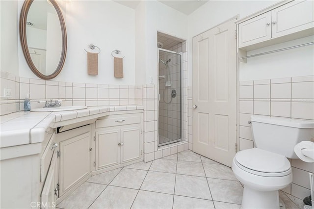 bathroom featuring toilet, vanity, tile walls, tile patterned floors, and a shower with shower door