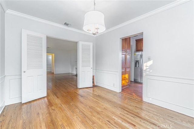 unfurnished dining area with light hardwood / wood-style flooring, crown molding, and a notable chandelier