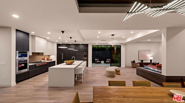 kitchen featuring a center island with sink, a raised ceiling, pendant lighting, a kitchen bar, and stainless steel appliances