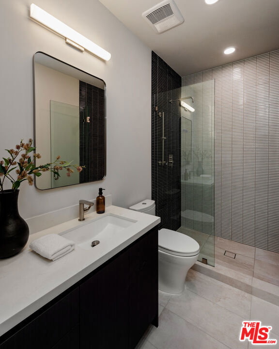 bathroom featuring toilet, vanity, tile patterned flooring, and a tile shower