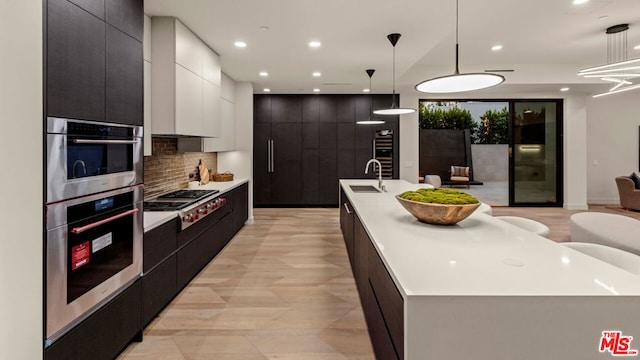 kitchen featuring decorative light fixtures, white cabinets, a large island with sink, and stainless steel gas stovetop