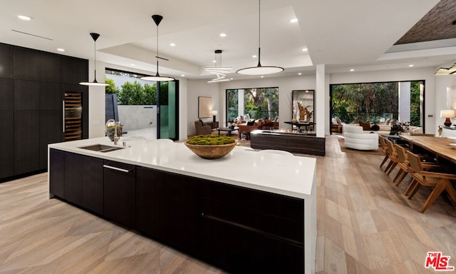 kitchen with sink, hanging light fixtures, a tray ceiling, and a large island with sink