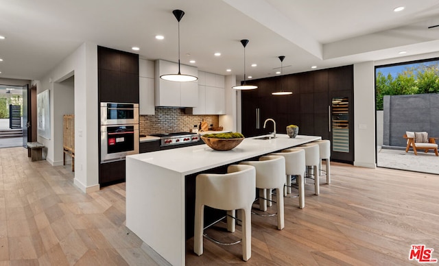 kitchen with backsplash, pendant lighting, a breakfast bar, white cabinetry, and a kitchen island with sink