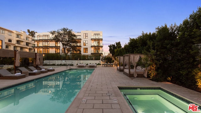 pool at dusk featuring a patio area and a community hot tub