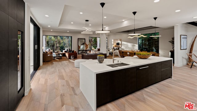 kitchen with decorative light fixtures, a kitchen island with sink, sink, and a raised ceiling