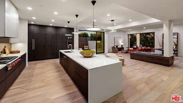 kitchen with stainless steel gas stovetop, hanging light fixtures, an island with sink, white cabinets, and dark brown cabinets