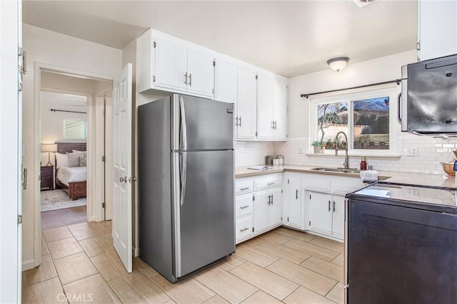 kitchen with stainless steel fridge, decorative backsplash, stove, white cabinets, and sink