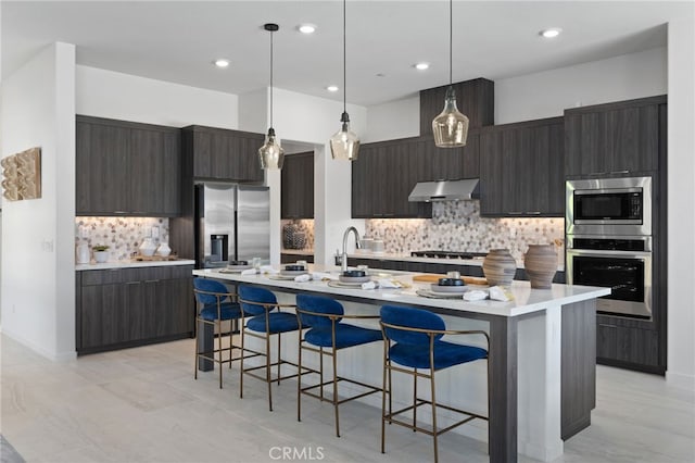 kitchen featuring appliances with stainless steel finishes, decorative light fixtures, a kitchen bar, tasteful backsplash, and a center island with sink