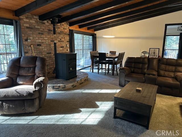 carpeted living room with a wood stove, vaulted ceiling with beams, and wood ceiling