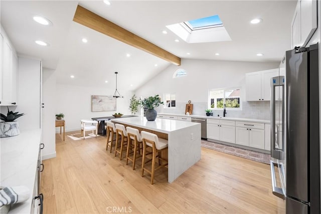 kitchen with decorative light fixtures, a kitchen island, white cabinetry, appliances with stainless steel finishes, and a kitchen breakfast bar