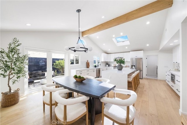 dining space with a skylight, beamed ceiling, sink, light wood-type flooring, and high vaulted ceiling