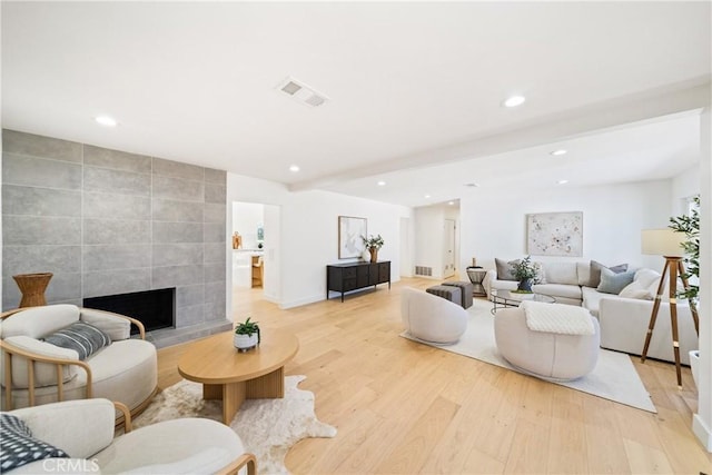 living room featuring tile walls, light hardwood / wood-style flooring, beam ceiling, and a fireplace