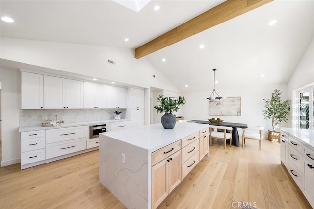 kitchen featuring pendant lighting, a center island, backsplash, light hardwood / wood-style flooring, and beam ceiling