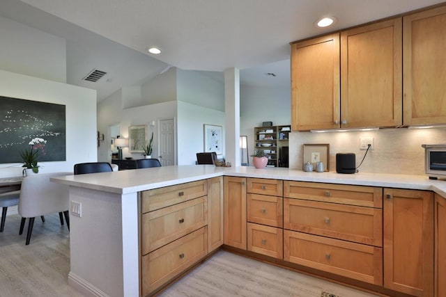 kitchen featuring vaulted ceiling, light hardwood / wood-style flooring, kitchen peninsula, and tasteful backsplash