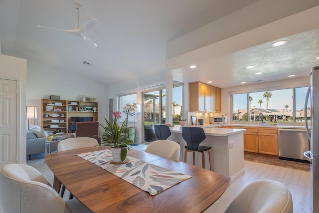 dining space with ceiling fan, a healthy amount of sunlight, vaulted ceiling, and light wood-type flooring