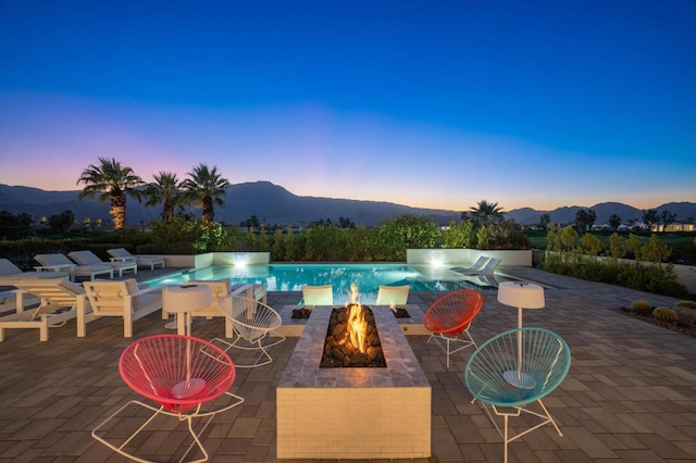 pool at dusk featuring a mountain view, an outdoor fire pit, and a patio