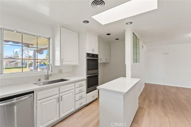 kitchen featuring sink, white cabinetry, a skylight, light wood-type flooring, and stainless steel appliances