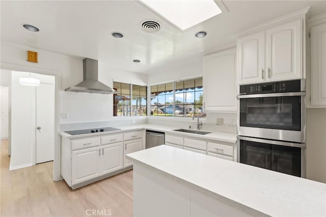 kitchen featuring stainless steel appliances, wall chimney exhaust hood, white cabinets, and sink