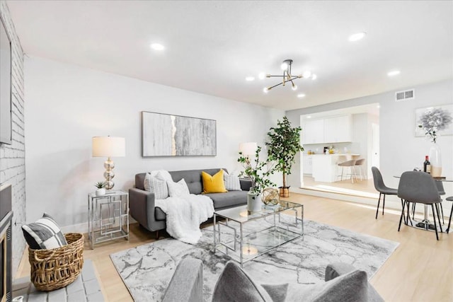 living room featuring light wood-type flooring, a brick fireplace, and an inviting chandelier