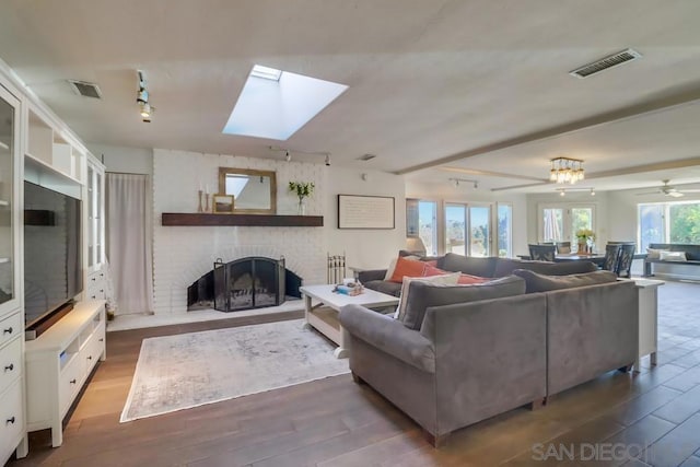 living room featuring ceiling fan, a skylight, a fireplace, and dark hardwood / wood-style floors