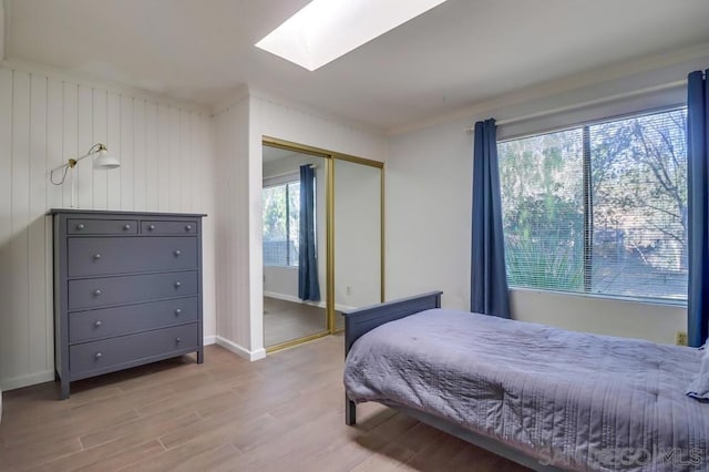 bedroom with multiple windows, a closet, a skylight, and light hardwood / wood-style flooring