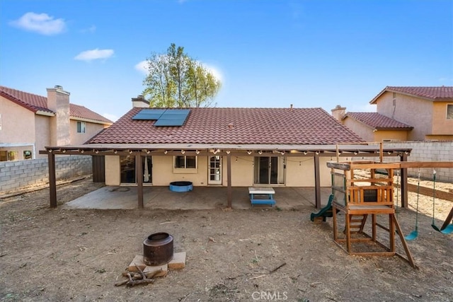 rear view of property with solar panels, a patio, and a playground