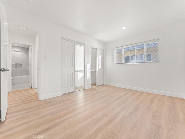 unfurnished bedroom featuring ensuite bath, light hardwood / wood-style flooring, and two closets