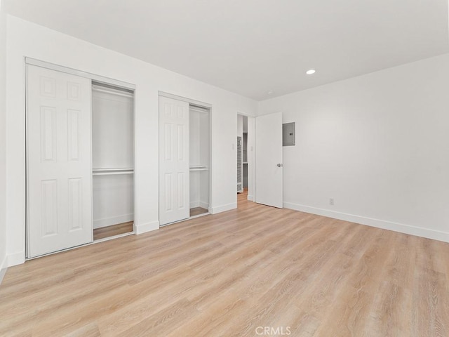 unfurnished bedroom with light hardwood / wood-style floors, two closets, and electric panel