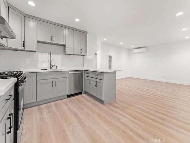 kitchen featuring wall chimney range hood, gray cabinets, kitchen peninsula, a wall mounted air conditioner, and appliances with stainless steel finishes