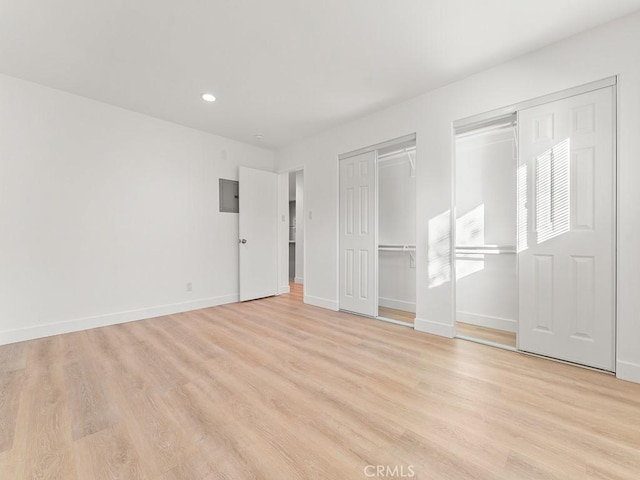 unfurnished bedroom with multiple closets, electric panel, and light hardwood / wood-style flooring