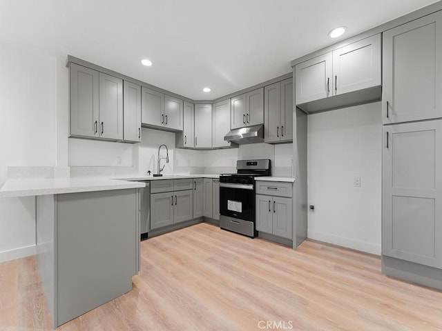 kitchen with gray cabinets, light hardwood / wood-style floors, a kitchen bar, kitchen peninsula, and stainless steel range with gas cooktop