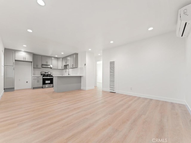 kitchen featuring gray cabinets, light hardwood / wood-style floors, a wall unit AC, stainless steel stove, and sink