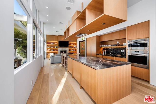 kitchen featuring a healthy amount of sunlight, dark stone countertops, light hardwood / wood-style flooring, and stainless steel double oven