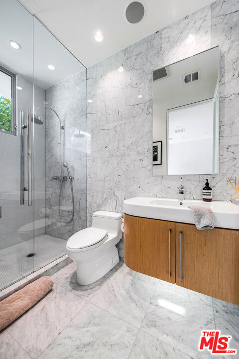 bathroom featuring a shower with shower door, tile walls, toilet, and vanity