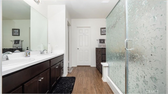 bathroom featuring double vanity, a stall shower, a sink, and wood finished floors