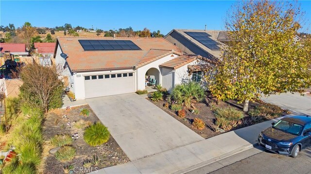 ranch-style house featuring a tile roof, stucco siding, an attached garage, roof mounted solar panels, and driveway