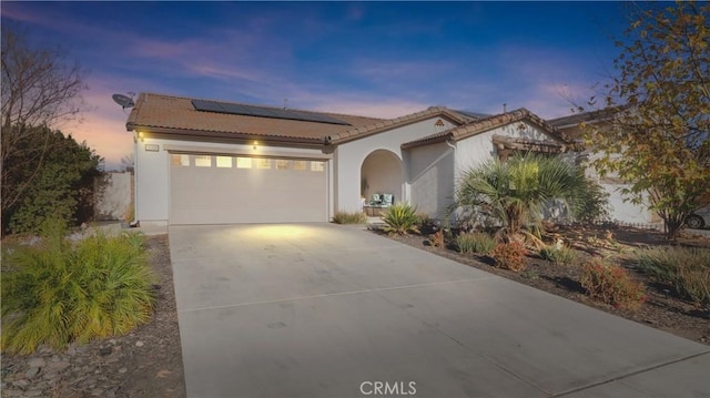 mediterranean / spanish-style home with concrete driveway, a tiled roof, an attached garage, roof mounted solar panels, and stucco siding