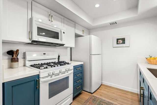 kitchen featuring white cabinetry, blue cabinetry, white appliances, and a tray ceiling