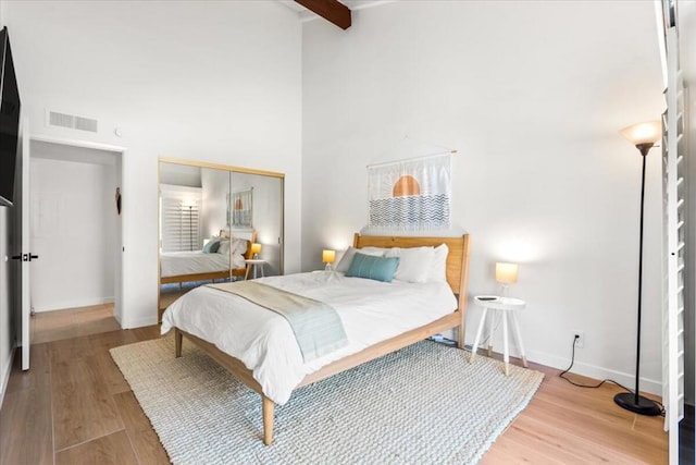 bedroom with light wood-type flooring, a closet, and beamed ceiling