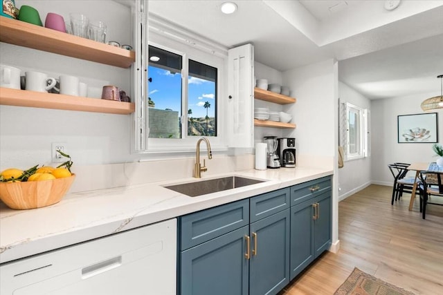 kitchen with pendant lighting, sink, light stone counters, light hardwood / wood-style flooring, and blue cabinets