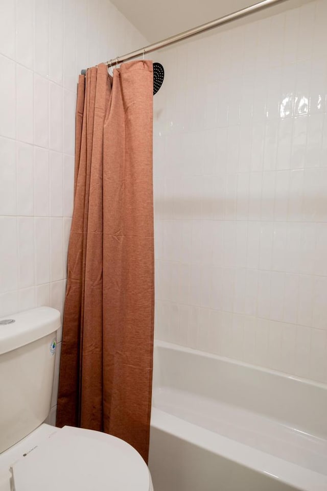 bathroom with toilet, tile walls, and shower / tub combo with curtain