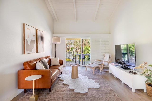 living room with a towering ceiling, hardwood / wood-style floors, and beamed ceiling