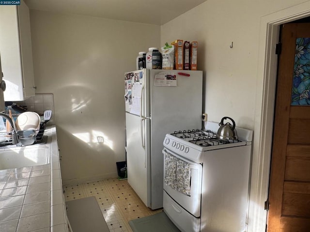 kitchen with sink, white appliances, white cabinets, and tile countertops