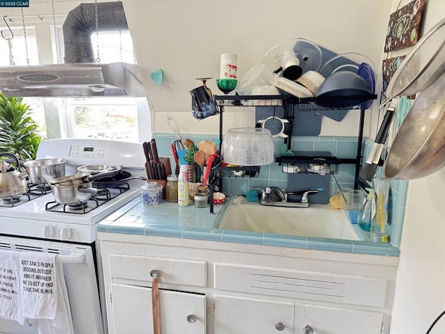 kitchen featuring sink, tile countertops, white gas range oven, and white cabinetry