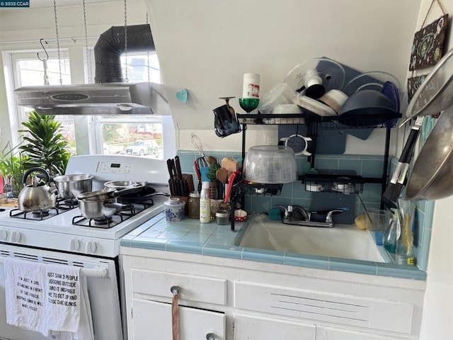 kitchen with extractor fan, sink, white gas range, tile counters, and white cabinets