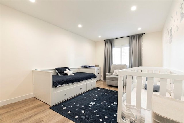 bedroom with light wood-type flooring and a nursery area