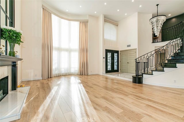 entrance foyer featuring light wood-type flooring, a high end fireplace, a wealth of natural light, and a notable chandelier